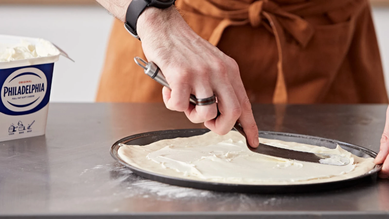 chef spreading cream cheese on sheet